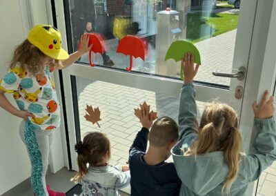 Kinder der Kita gestalten die Fenster des Eingangsbereiches herbstlich